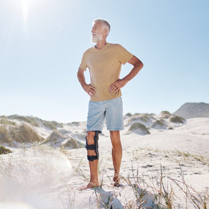 Ein Mann mit einer Knieorthese steht am Strand