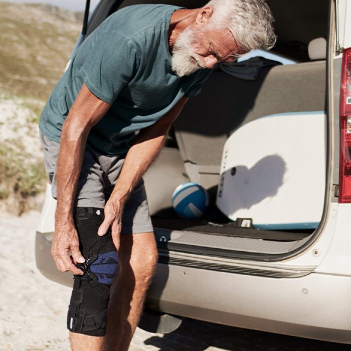 Älterer Herr befestigt neben seinem Auto seine Kniebandage