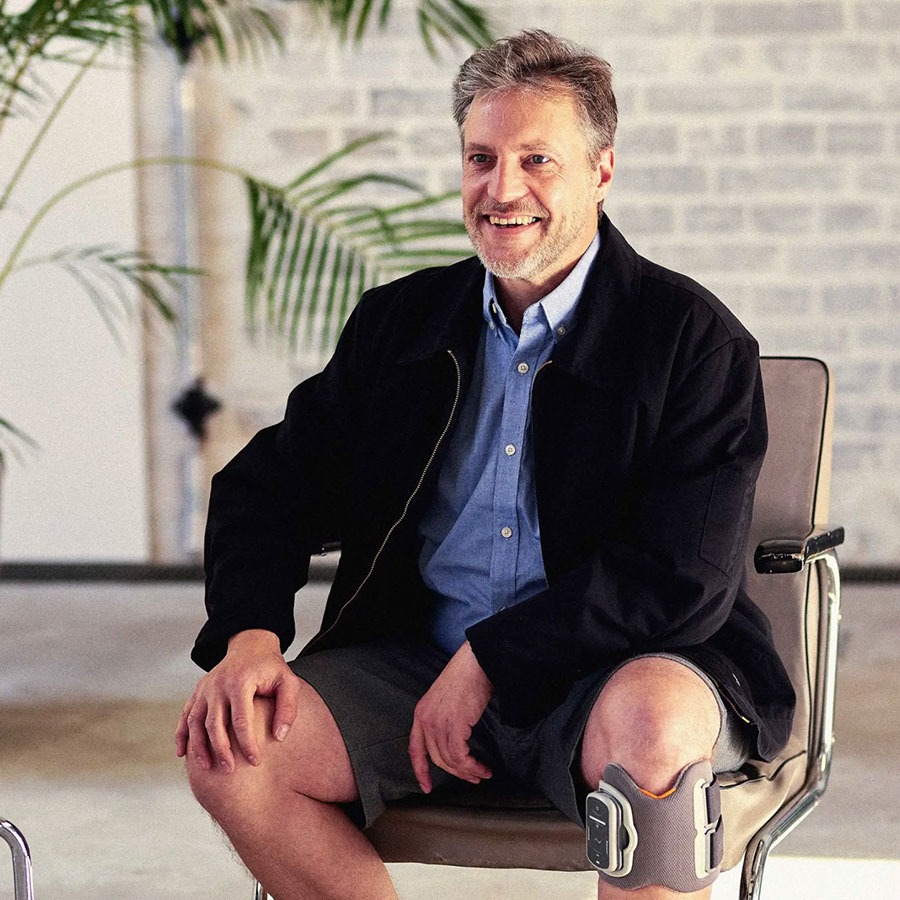 Mann sitzt lachend auf dem Stuhl mit einer Orthese wegen einer Fußheberbeschwerde
